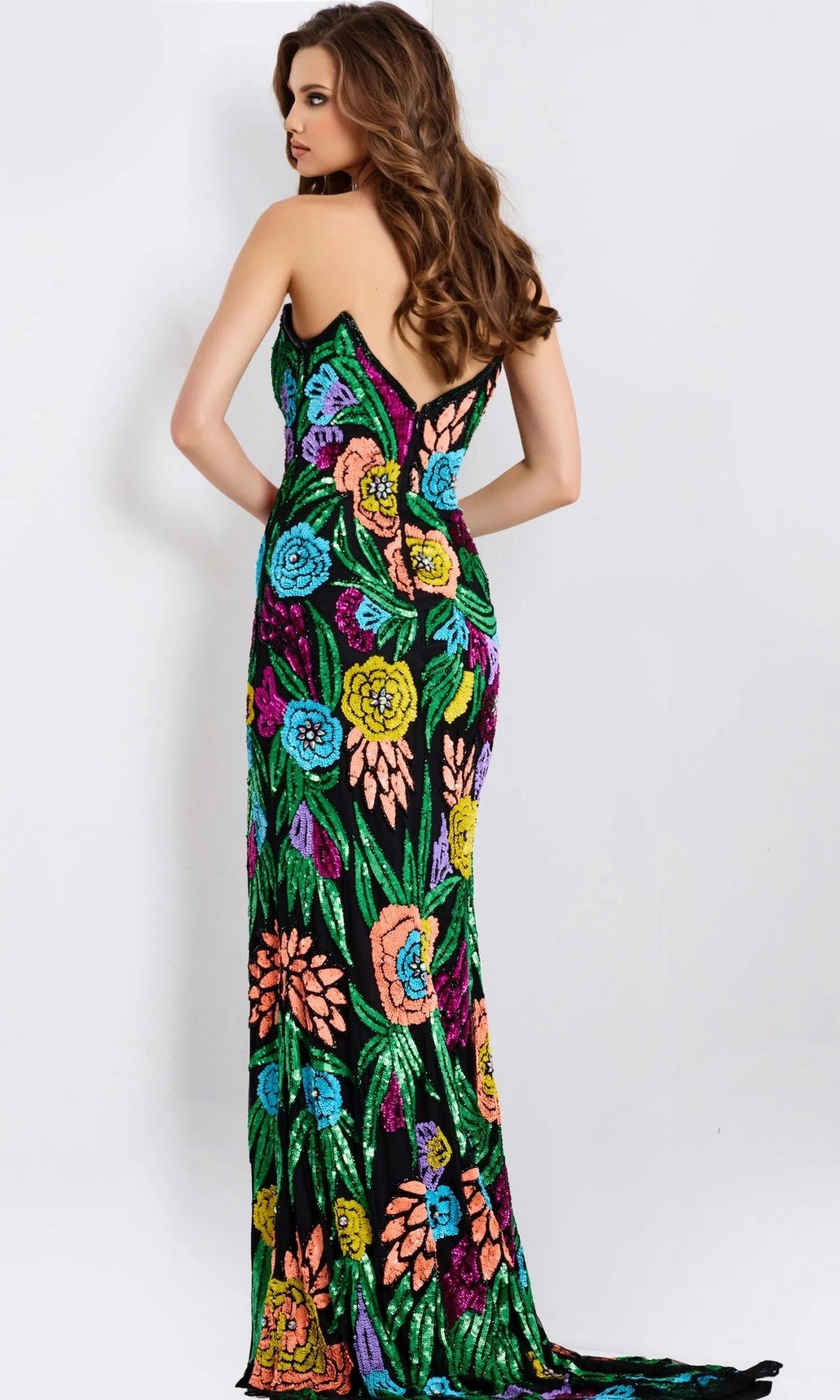 A woman faces away in a Jovani 49234 long prom dress—strapless, fitted, floor-length, black with colorful floral patterns—and looks over her shoulder.